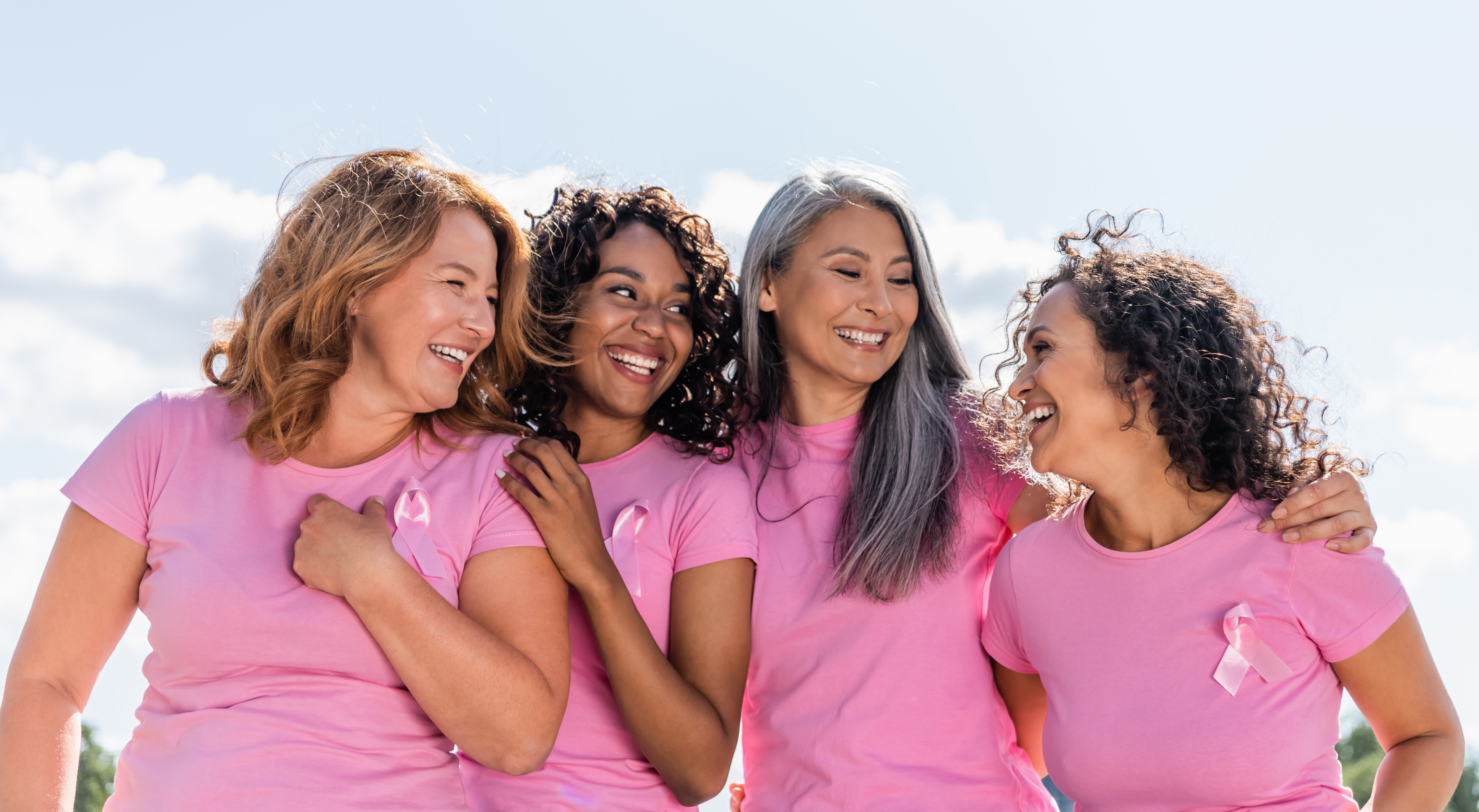 Group of women wearing pink and pink ribbon pins smiling.